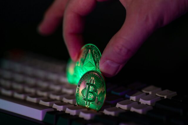 Photo by Jakub Żerdzicki Hand placing glowing crypto coins on a keyboard.